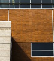 Fachada de edificio moderno con detalles en ladrillo naranja y paneles de vidrio. La imagen muestra la textura del ladrillo y la estructura arquitectónica contemporánea.