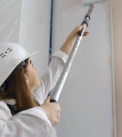 Mujer con casco de seguridad pintando una pared con rodillo en un espacio de construcción.